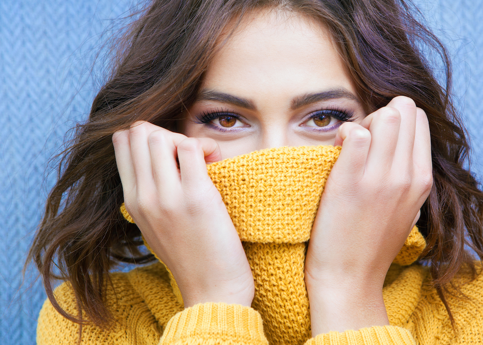 Woman covering mouth with sweater representing attempt to retreat from overstimulation for the highly sensitive person